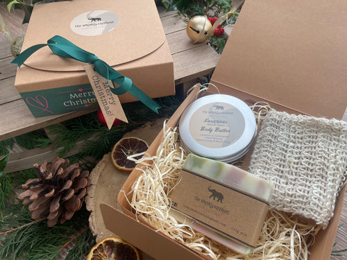 Natural handmade body butter, along with a natural soap bar and exfoliating jute bag in a Christmas gift box with ribbon and gift tag.