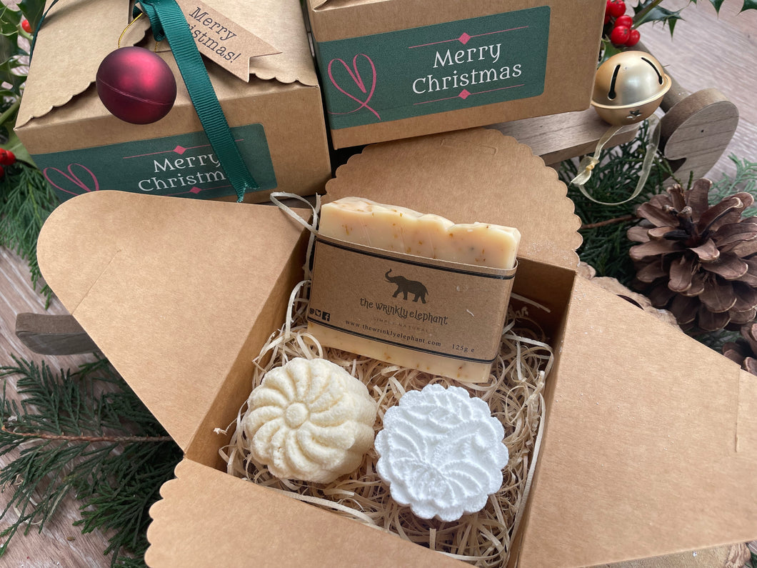 Gift set with natural handmade soap and aromatherapy shower steamers in a decorative box with Christmas-themed elements.